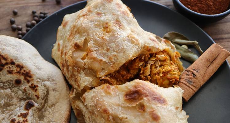 Gros plan d'une pâtisserie feuilletée fourrée au poulet à la sauce curry sur une assiette noire.
