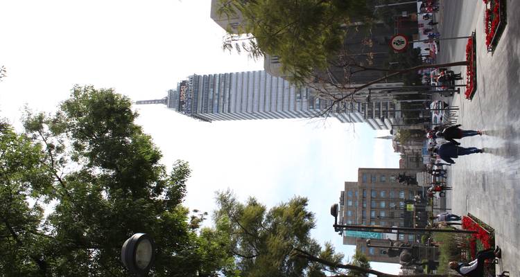 Straßenszene mit dem Torre Latinoamericana, der sich über Fußgänger und Blumenbeete erhebt