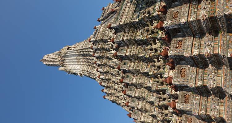 Primer plano de la imponente prangs del Wat Arun mostrando sus intrincados pisos bajo un cielo azul.