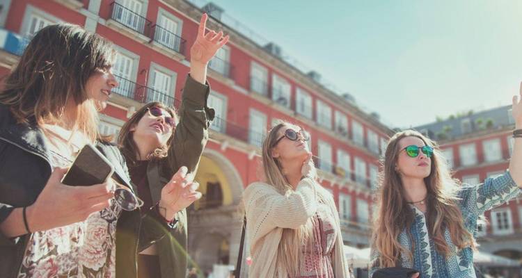 Group of young women pointing out sights in Madrid's historic red-walled Plaza Mayor.