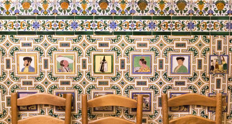 Decorative Andalusian ceramic tile wall featuring portrait motifs above wooden chairs.