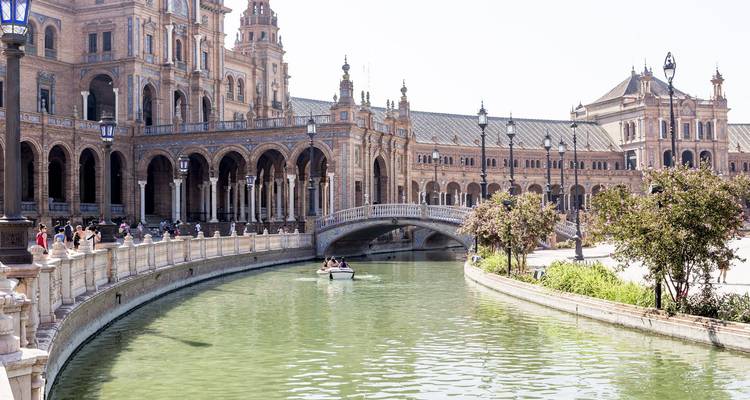 Canal boat glides beneath ornate bridges of Seville's Plaza de España amid the expansive square.