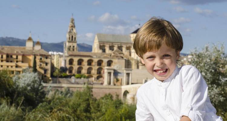 Un jeune garçon souriant avec la Mezquita de Cordoue et l'horizon de la ville légèrement flous derrière lui.