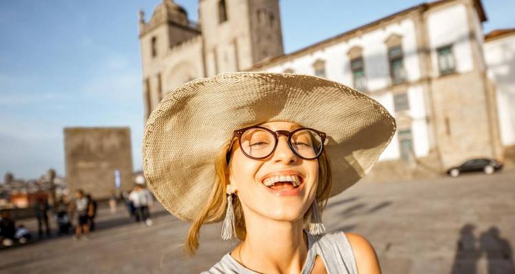 Mujer sonriente con sombrero ancho tomándose una selfie frente a la Catedral de Oporto bajo una luz cálida.