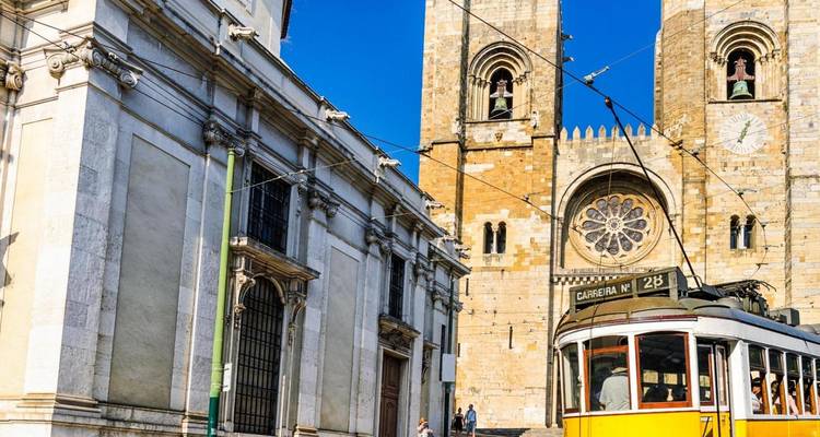 El tranvía amarillo pasa por la Catedral de Lisboa con sus dos torres contra un cielo azul intenso.