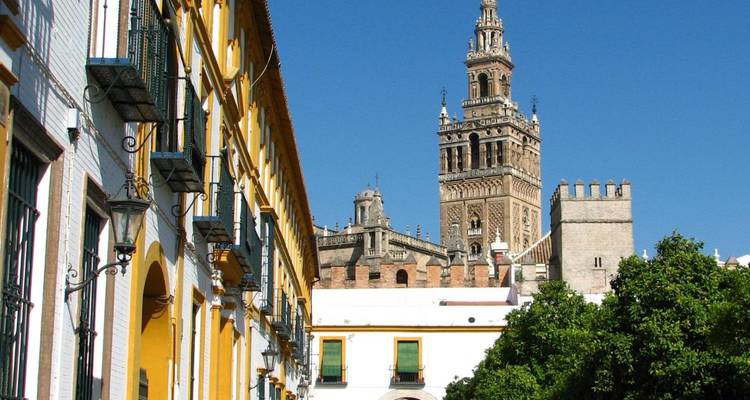 Street lined with colorful façades leading toward the Giralda tower under a vivid blue sky