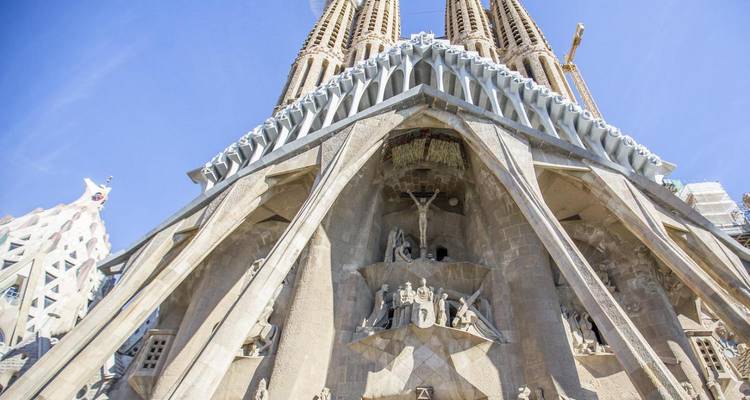 Upward perspective of the sculpted stone façade and soaring towers of the Sagrada Familia against a clear sky