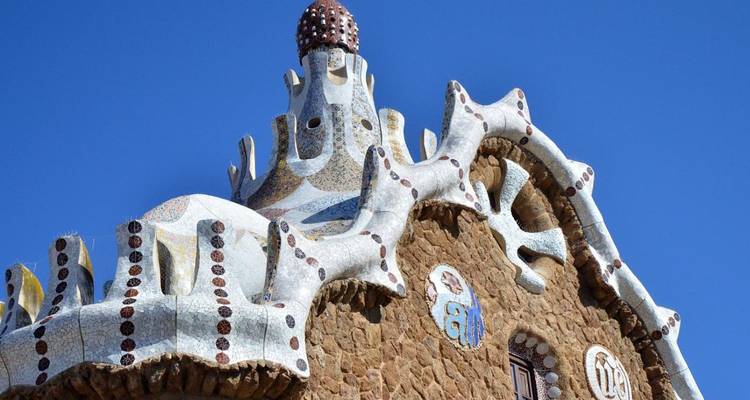 Colorful mosaic-covered gingerbread style roofline of a Gaudí house against clear blue sky