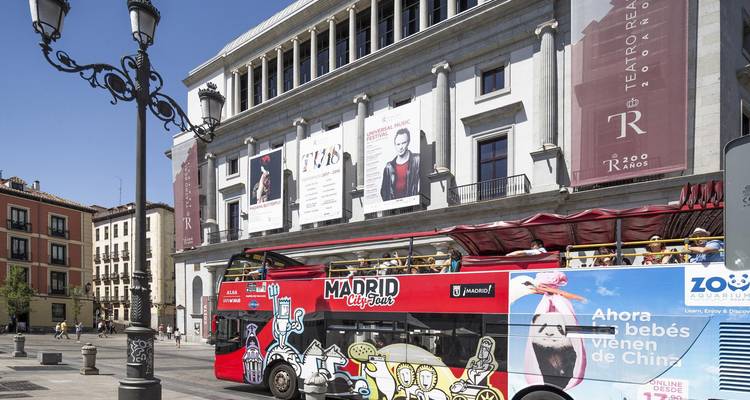 Open-top red city sightseeing bus passing the neoclassical Royal Theatre in a lively plaza