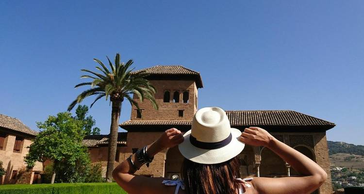 Mujer con sombrero admirando una torre de ladrillos y una palmera en los jardines de la Alhambra.