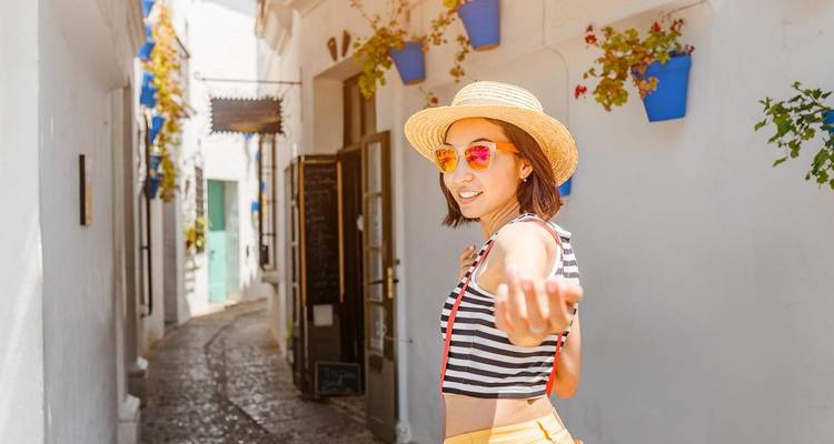 Mujer sonriente haciendo gestos juguetonamente en un callejón blanco andaluz decorado con macetas azules.