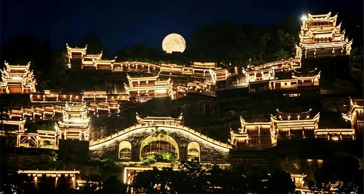 La luna llena se eleva sobre un antiguo pueblo extenso iluminado con linternas y un puente de piedra arqueado de noche.