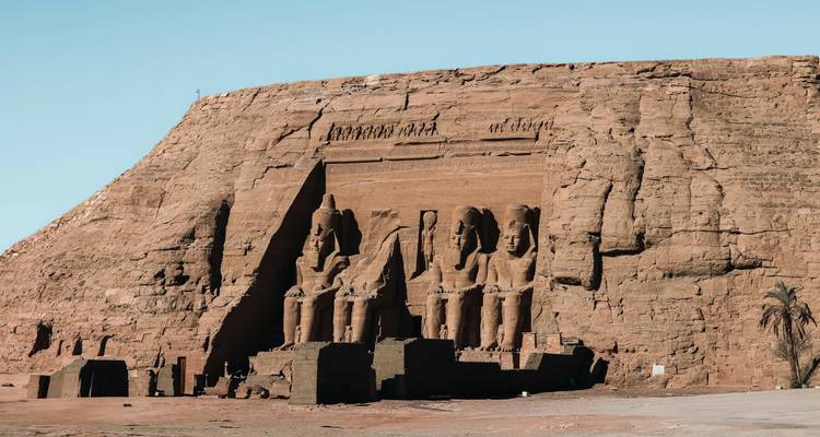 Des statues colossales assises sculptées dans la paroi rocheuse à Abu Simbel sous un ciel bleu dégagé.