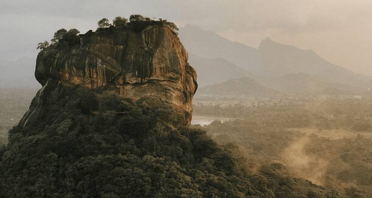 Vista aérea con ambiente misterioso de la Roca de Sigiriya al amanecer rodeada de un paisaje boscoso y brumoso.