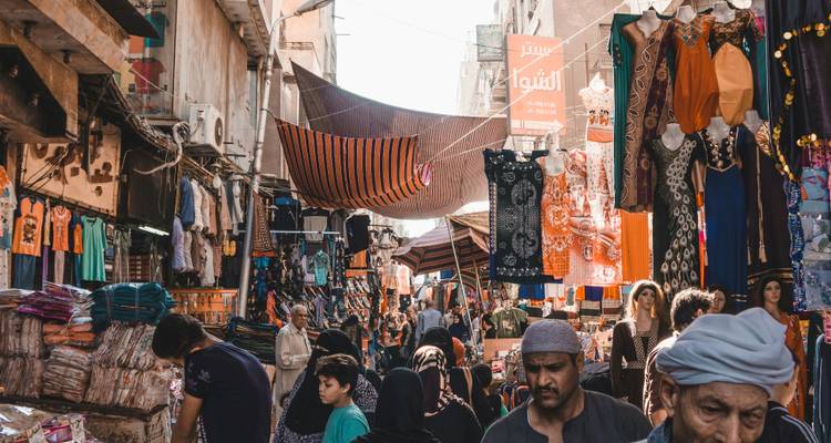 Bazar égyptien animé avec des tissus suspendus, des étals bondés et des clients sous des auvents rayés