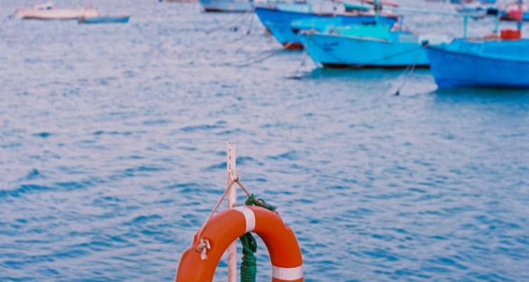 Bouée de sauvetage orange accrochée à la rampe avec des bateaux bleus amarrés légèrement flous en arrière-plan