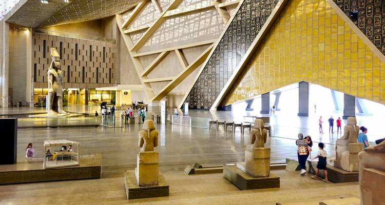 Geräumige Halle eines modernen ägyptischen Museums mit pharaonischen Statuen und Besuchern, die umhergehen.
