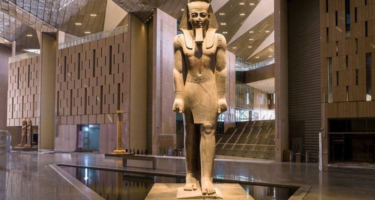 Large ancient pharaoh statue displayed inside a modern museum hall.