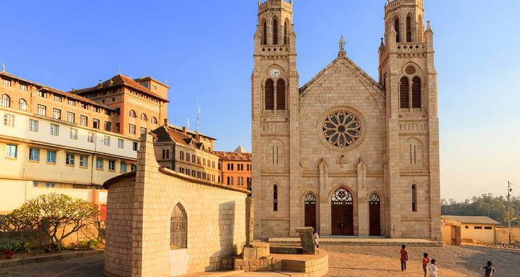 Catedral de piedra gótica con dos torres gemelas bañadas por la cálida luz de la tarde, con algunos lugareños caminando cerca.