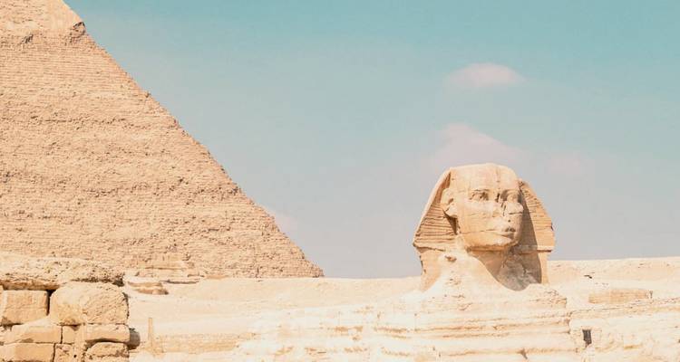 Classic view of the Great Sphinx with a pyramid rising beside it under a clear sky.