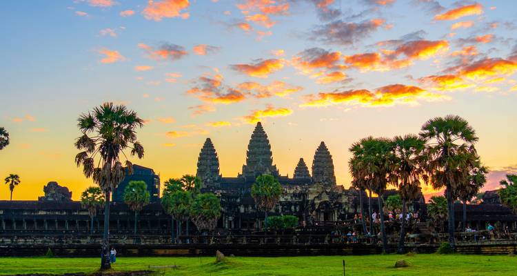 Angkor Wat recortado contra un cielo de amanecer vibrante con palmeras en primer plano.