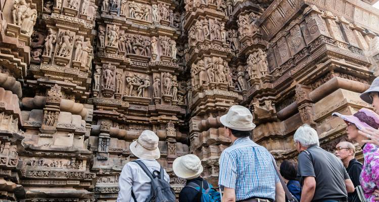 Eine Reisegruppe studiert detaillierte Steinschnitzereien an den Mauern des Khajuraho-Tempels.