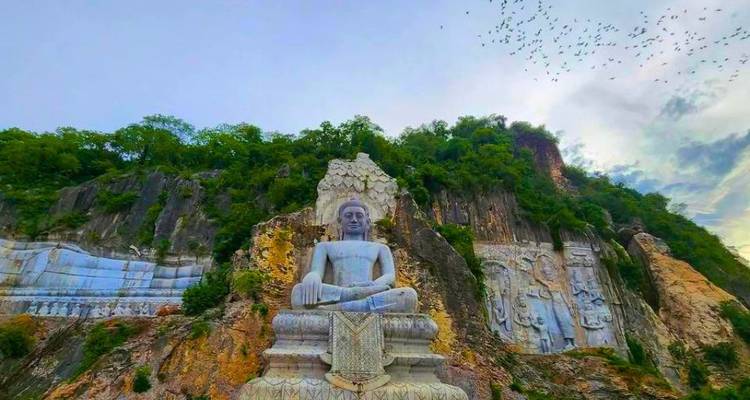 Enorme estatua de Buda sentado tallada en un acantilado de piedra caliza con relieves circundantes y vegetación