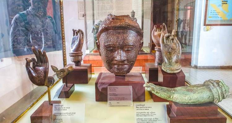 Reliquias de bronce antiguo, incluyendo una cabeza esculpida y fragmentos de manos, exhibidas en una vitrina de museo de cristal.