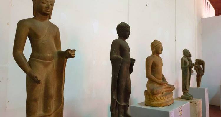 Una fila de estatuas de piedra jemer alinea suavemente una pared de galería de museo iluminada.