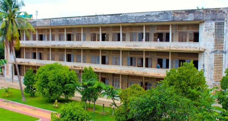 Los bloques de hormigón desgastados del Museo del Genocidio de Tuol Sleng se alzan detrás de unos árboles frondosos.