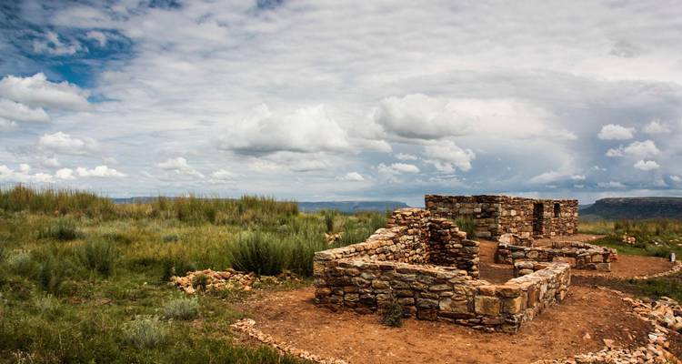 Ruines d'une ancienne structure en pierre s'élevant dans une plaine herbeuse sous un ciel nuageux aux textures variées.