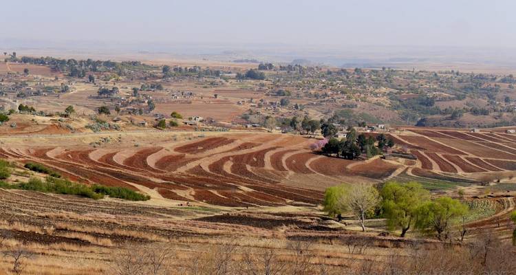 Patchwork de terres agricoles en terrasses de couleur brun rougeâtre s'étendant vers un lointain établissement rural sur le plateau.
