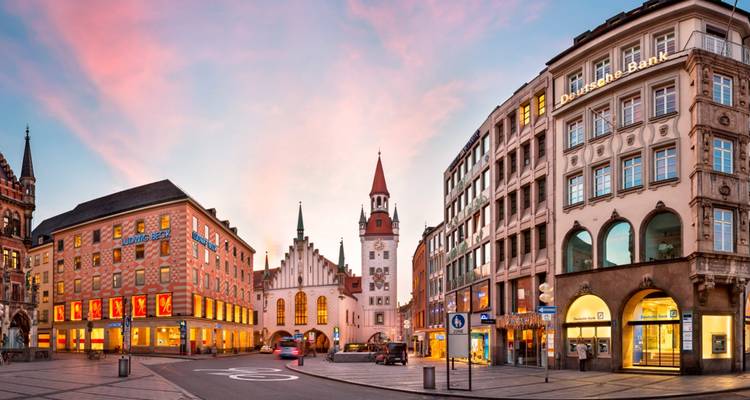 Escena vibrante de la calle del casco antiguo de Munich al atardecer con cielo pastel y edificios históricos iluminados calurosamente.