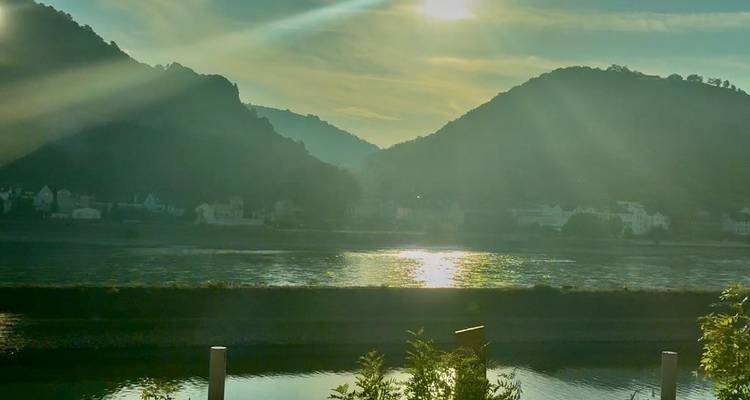 Vista ribereña llena de brillo al atardecer con colinas recortadas y agua brillante.