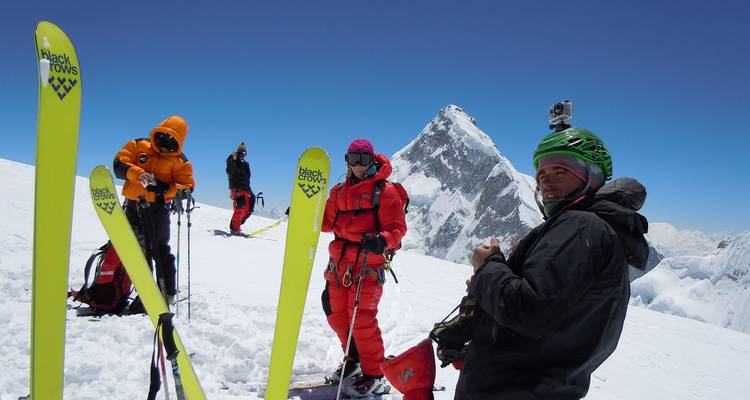 High-altitude ski mountaineers posing on a snowy summit with sharp peaks behind them