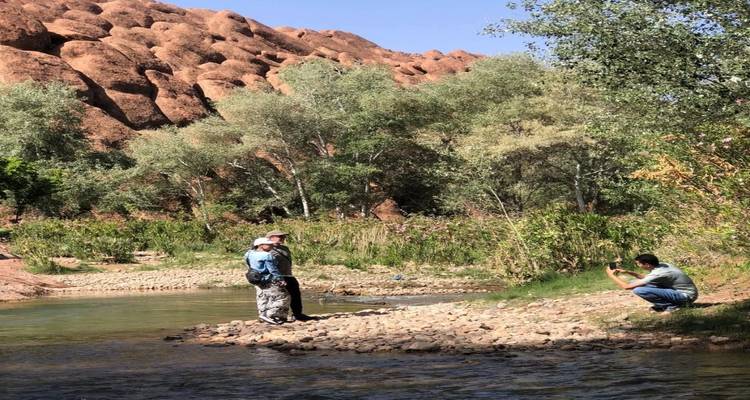 Les voyageurs se détendent au bord d'une rivière peu profonde avec des formations rocheuses rouges spectaculaires en arrière-plan