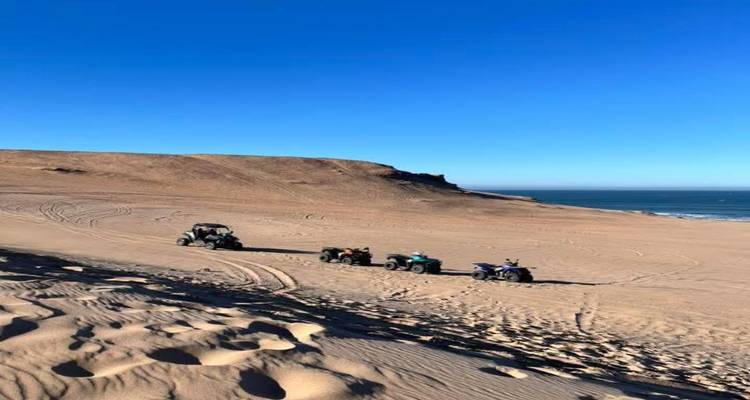 Des quads stationnés sur de vastes dunes de sable côtières sous un ciel bleu dégagé