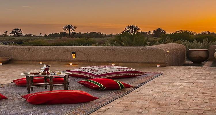 Terrasse sur le toit aménagée de coussins de sol colorés et de lanternes au coucher de soleil sur les palmeraies
