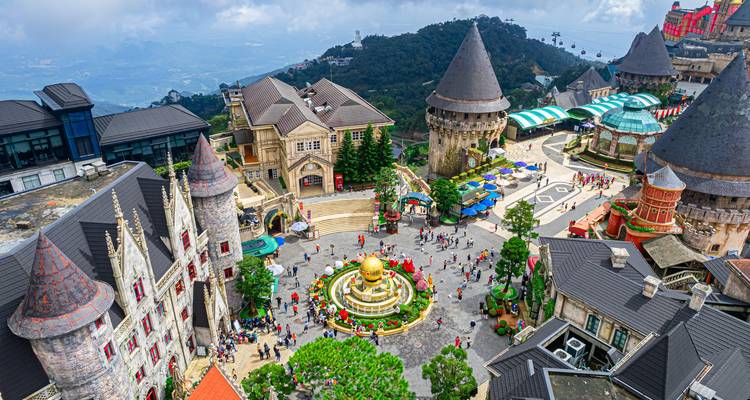 Eine Luftaufnahme des französischen Dorfes Ba Na Hills zeigt verspielt gestaltete Gebäude mit Türmchen, Plätze und lebhafte Besucher.
