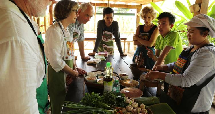 Los participantes del tour se reúnen alrededor de una mesa de madera cubierta de ingredientes frescos durante una clase de cocina laosiana.