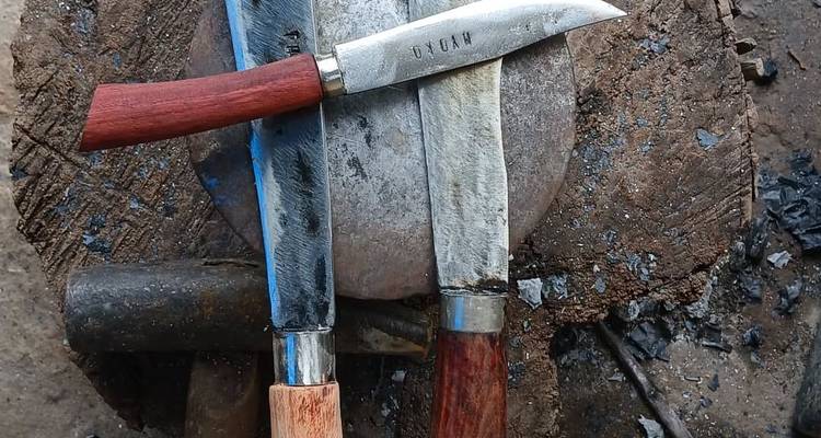 Tres cuchillos hechos a mano dispuestos en un bloque de madera al lado de un martillo en una herrería.