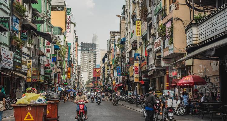Belebte asiatische Stadtstraße mit hohen Gebäuden, Motorrädern und farbenfrohen Schildern