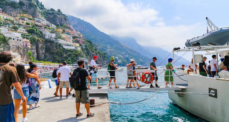 Passagiers stappen aan boord van een klein bootje bij de pier van Positano met kleurrijke huizen aan de klif op de achtergrond.