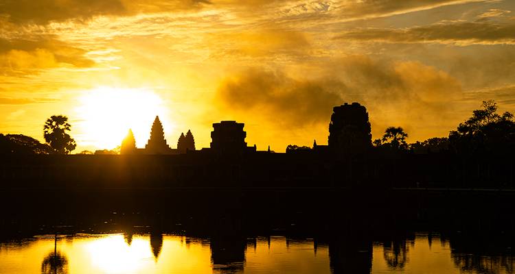 Silhouette of Angkor Wat reflected in a pond at fiery sunrise
