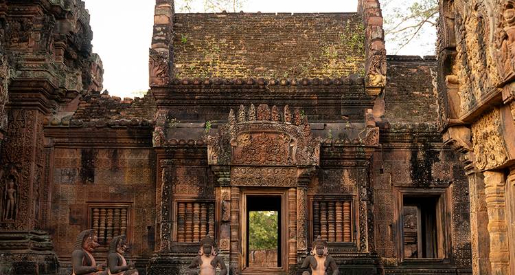 Intricately carved doorway and statues at a reddish sandstone Khmer temple