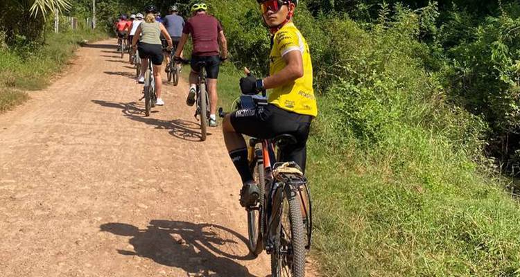 Cyclists riding along a dusty rural road surrounded by greenery