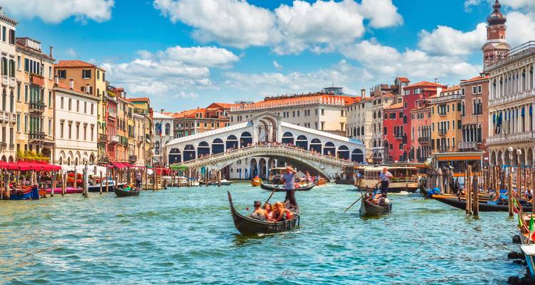 Klassische Ansicht des Großkanals von Venedig mit Gondeln, die unter blauem Himmel in Richtung der Rialtobrücke gleiten.