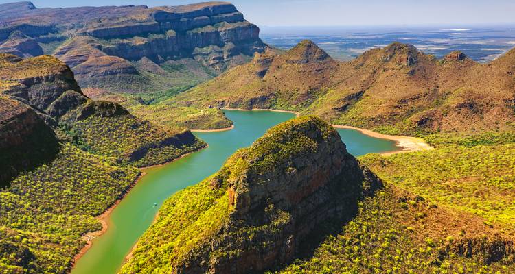 Vista aérea del sinuoso río verde y las escarpadas crestas de montaña anaranjadas del Cañón del Río Blyde bajo cielos despejados.