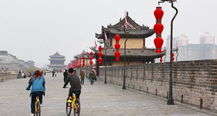 Fietsers rijden langs de oude stadsmuur van Xi'an met rode lantaarns en grijze stenen kantelen.
