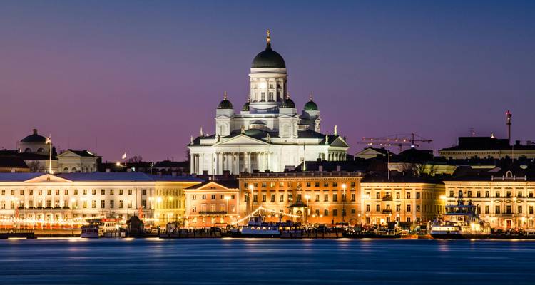 Dusk panorama across the harbor toward Helsinki’s illuminated waterfront and cathedral under a violet twilight sky.